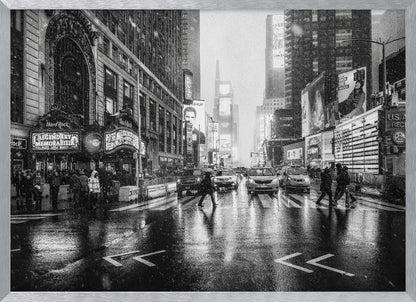 A moody black and white photograph of a snowy day in New York City's Times Square. The wet streets reflect the bright lights of the surrounding buildings and billboards as pedestrians cross the street and cars wait in traffic. Artwork