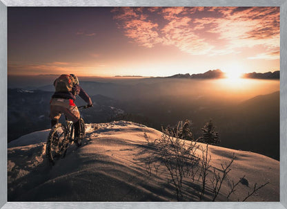 A mountain biker seen from behind pauses on a snowy mountain summit, overlooking a vast, misty mountain range as the sun sets, casting a warm orange and pink glow across the sky and snow. Artwork