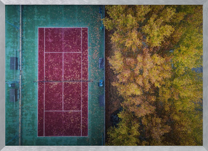 An aerial top-down photograph of a red and green tennis court covered in fallen leaves, adjacent to a dense grove of trees with vibrant yellow and gold autumn foliage, all enclosed in a silver frame. Wall Art