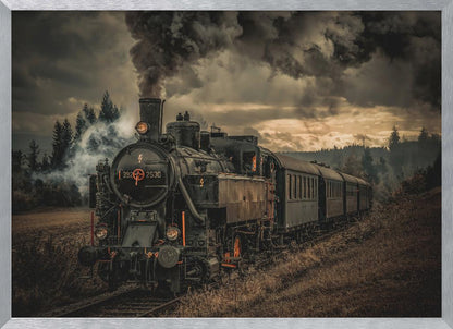 A powerful black steam locomotive on a railway track, billowing thick dark smoke into a dramatic, cloudy sky. The train travels through a rustic, grassy landscape, and the image has a warm, vintage color tone, all within a silver frame. Wall Art