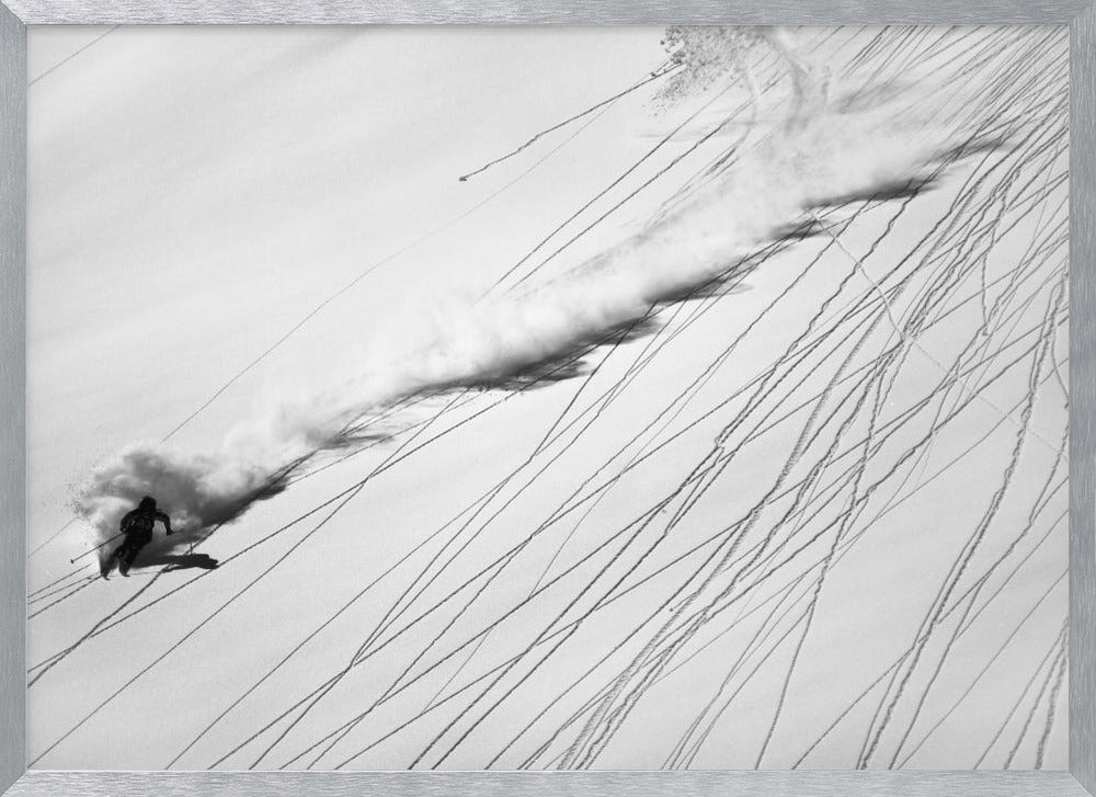 A dramatic black and white overhead photograph of a skier carving down a steep, powder-filled mountain slope, kicking up a huge plume of snow. Numerous ski tracks crisscross the pristine white snow, creating a pattern of dark lines. Poster