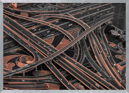 A framed aerial photograph of a sprawling, multi-level highway interchange presented in a selective color style. Dark grey roads weave over and under each other, while the surrounding land is a contrasting copper-brown, creating a dramatic and complex urban pattern. Poster