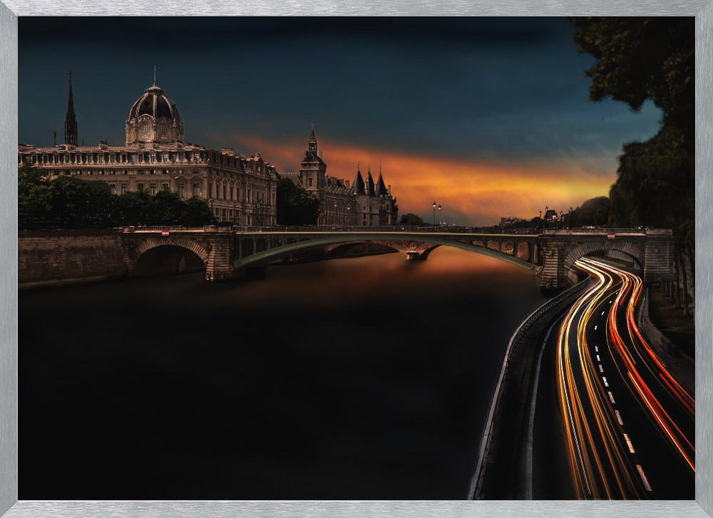 A dramatic long-exposure photograph of Paris at dusk, featuring historic buildings and a bridge over the Seine, with glowing light trails from traffic on a winding riverside road under a vibrant orange and dark blue sky. Wall Art