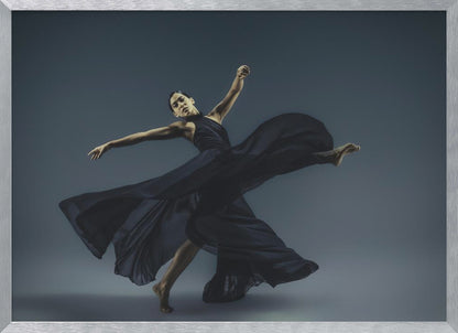 A framed photograph of a graceful female dancer in a dramatic pose, her long, dark blue, flowing dress billowing around her against a muted blue-gray studio background. Wall Art