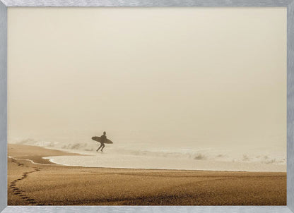 A minimalist photograph of a silhouetted surfer carrying a surfboard, running into the ocean on a foggy morning. The scene has a warm, sepia tone, with footprints visible in the wet sand in the foreground and a vast, misty sky. Wall Art