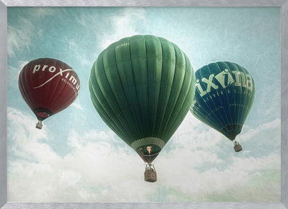 A low-angle photograph of three colorful hot air balloons floating in a cloudy blue sky, presented in a silver frame. A large green balloon is in the center, with a red balloon on the left and a dark blue balloon on the right, all featuring logos. Wall Art