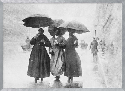 A vintage black and white photograph in a silver frame, depicting three people in long dark coats walking together under umbrellas during a heavy snow or rain storm on a city street. The image has a grainy, textured quality, giving it an old-fashioned, artistic feel. Poster