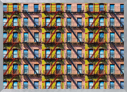 A pop-art style repeating pattern of a colorful apartment building facade featuring pink and yellow walls, windows reflecting a blue sky, and a network of black and red fire escapes, enclosed in a silver frame. Artwork