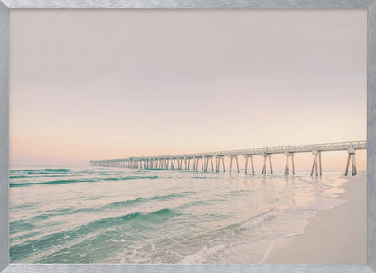 A tranquil beach scene with a long white pier extending into the turquoise ocean. The sky is a soft, pale pink, suggesting a serene sunrise or sunset, and gentle waves lap onto the sandy shore in the foreground. Poster
