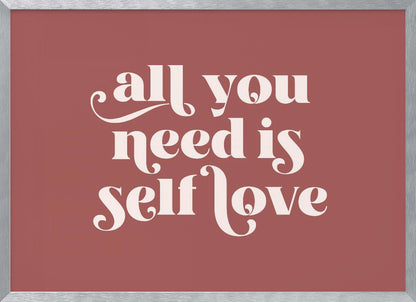 A framed art print with a dusty rose background. In the center, the phrase 'all you need is self love' is written in a creamy white, stylized, retro font. The artwork is enclosed in a simple silver frame. Decor