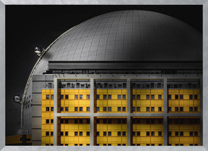 A framed architectural photograph with selective color, featuring a bright yellow building in the foreground against a monochrome background of a large grey dome structure under a black sky. Wall Art