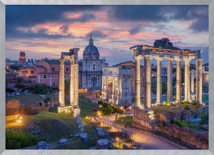 A scenic photograph of the ancient Roman Forum in Rome, Italy, at dusk. The ruins, including prominent columns and arches, are illuminated by warm lights, contrasting with the deep blue and vibrant pink of the sunset sky. Wall Art