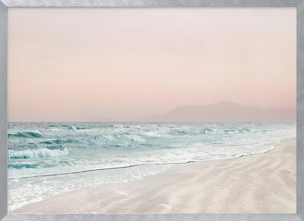 A serene coastal scene with gentle turquoise waves washing onto a sandy beach. The sky is a soft, hazy pink, and faint outlines of mountains are visible in the distant background. The artwork is presented in a silver frame. Print