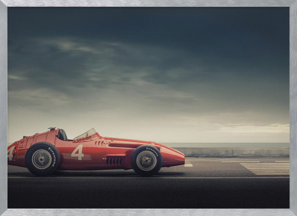 A side profile of a vintage red single-seater race car with the number 4 painted on it, parked on a seaside road under a dramatic, cloudy sky. The image has a muted, nostalgic color palette and is shown within a silver frame. Decor