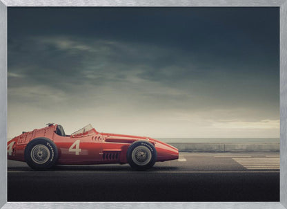 A side profile of a vintage red single-seater race car with the number 4 painted on it, parked on a seaside road under a dramatic, cloudy sky. The image has a muted, nostalgic color palette and is shown within a silver frame. Decor