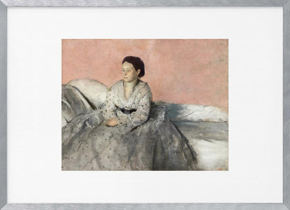 A framed impressionist painting of a woman with dark hair sitting on a bed against a dusty rose background. She wears a white, dotted blouse and a voluminous gray skirt, looking thoughtfully to her left. The painting is set in a silver frame with a white mat. Poster