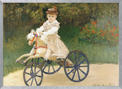 An Impressionist painting by Claude Monet depicting his son, Jean, riding a toy horse tricycle. The young boy wears a brown hat and a light-colored outfit, sitting on a white hobby horse with large blue wheels, set against a lush green garden background. Decor