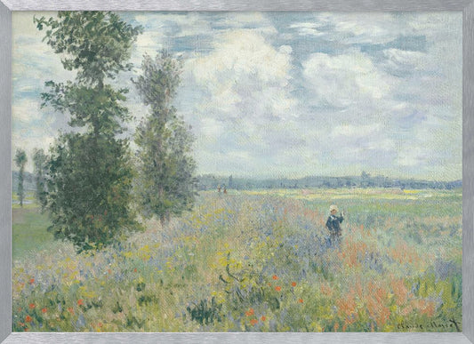 An impressionist painting by Claude Monet titled 'Poppy Field near Vétheuil', depicting a vast field of green grass dotted with red, yellow, and purple wildflowers. A figure in a white bonnet stands in the field to the right. Tall green trees are on the left, under a blue sky with fluffy white clouds. The entire scene is presented within a modern silver frame. Wall Art