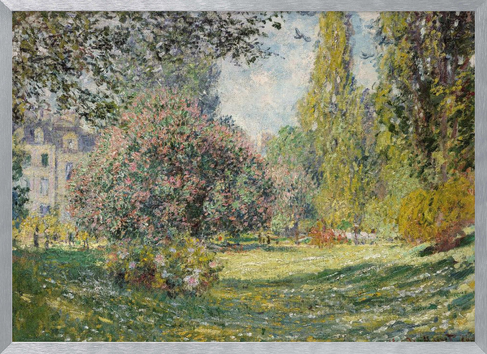 An impressionist painting by Claude Monet titled 'The Parc Monceau' displayed in a silver frame. The scene depicts a sunlit park with lush green grass, a large pink-flowering bush, and tall, leafy trees under a pale blue sky. Decor