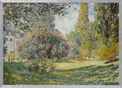 An impressionist painting by Claude Monet titled 'The Parc Monceau' displayed in a silver frame. The scene depicts a sunlit park with lush green grass, a large pink-flowering bush, and tall, leafy trees under a pale blue sky. Decor