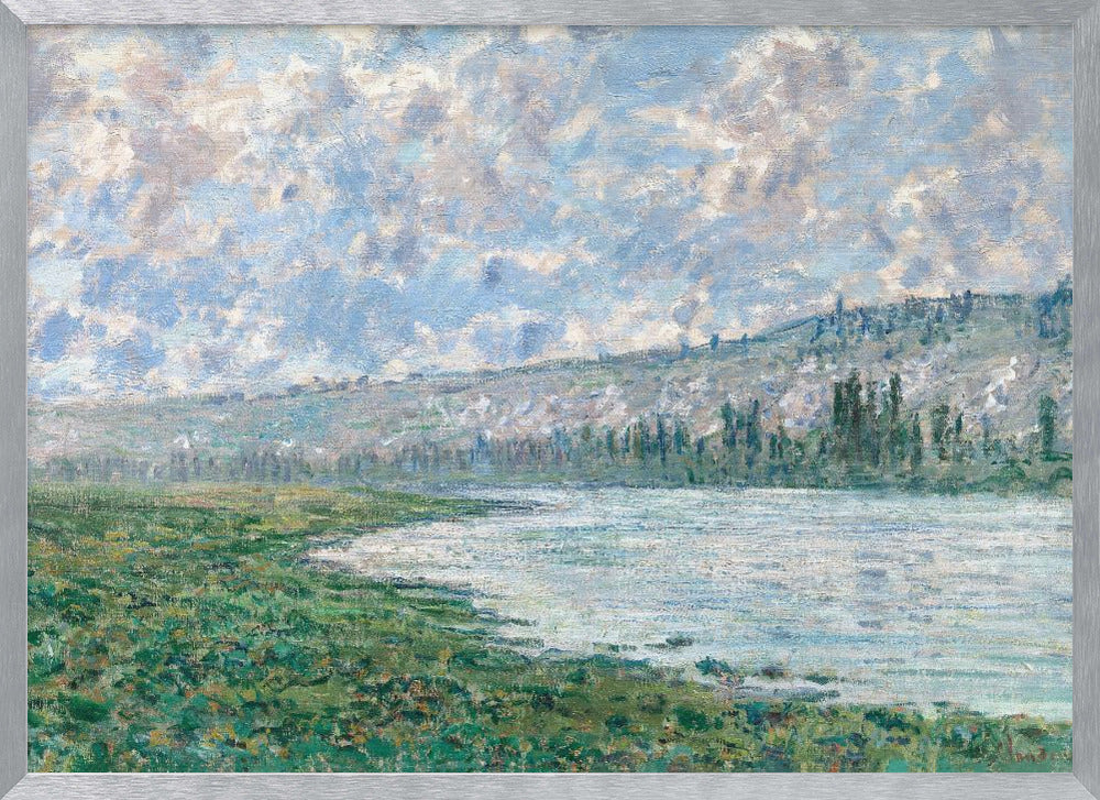 An Impressionist painting by Claude Monet, 'The Seine at Vétheuil', depicting a tranquil landscape. In the foreground, a lush green riverbank meets the calm, reflective water. A distant, soft-focus hillside rises under a vast sky filled with puffy white and grey clouds against a light blue background. The artwork is characterized by visible, textured brushstrokes and is displayed in a modern silver frame. Artwork