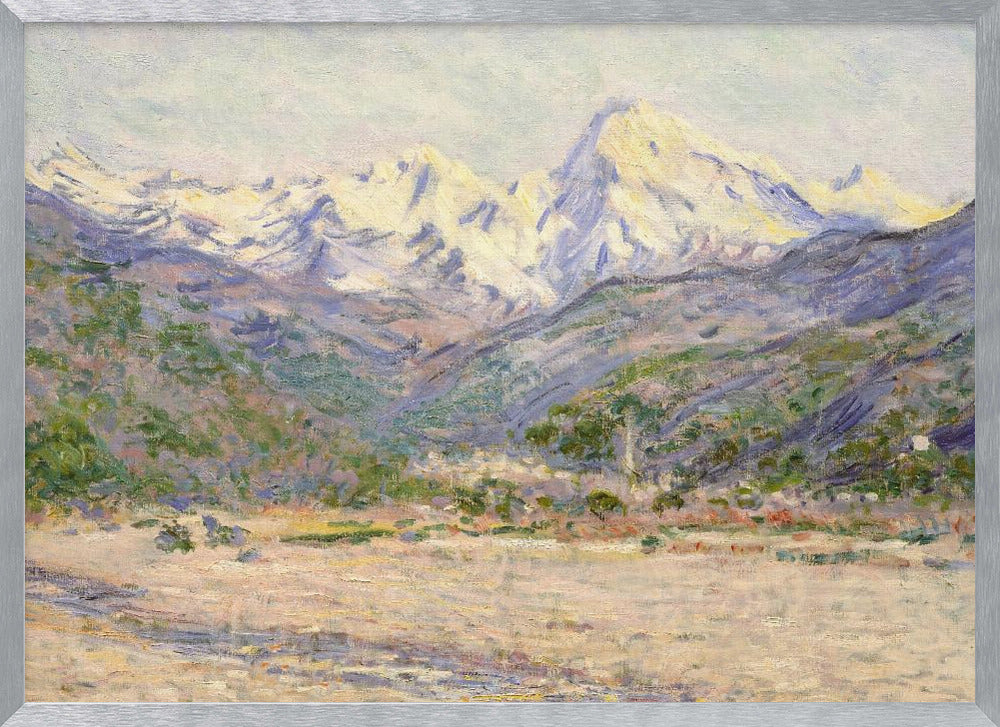 An impressionistic painting of a vast mountain range. The snow-covered peaks are bathed in pale yellow sunlight, while the lower slopes are cast in shades of purple and blue. A wide, beige valley with patches of green foliage sits in the foreground, all rendered with visible, textured brushstrokes and displayed in a silver frame. Print