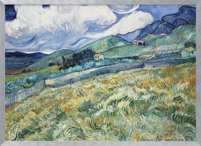A framed Post-Impressionist painting by Vincent van Gogh depicting a vibrant, rolling landscape. The foreground is filled with swirling brushstrokes of green and yellow fields, leading back to green hills dotted with small houses. In the background, dark blue mountains rise up to meet a dramatic sky filled with large, swirling white clouds against a deep blue. Wall Art