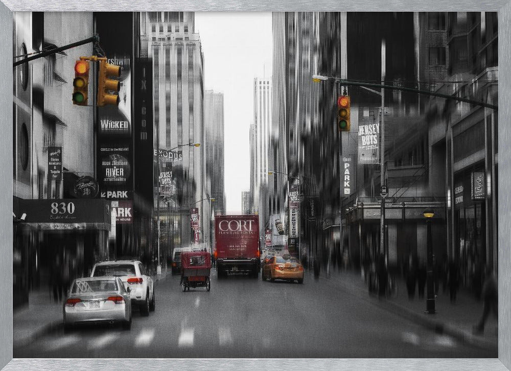 A framed, stylized photograph of a busy New York City street, presented mostly in black and white with a motion blur effect. Pops of color highlight red vehicles and yellow traffic lights, drawing focus down the urban canyon lined with skyscrapers and Broadway signs. Decor