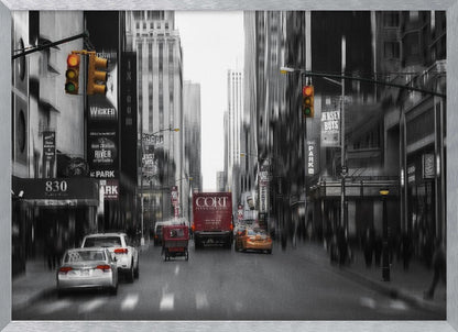 A framed, stylized photograph of a busy New York City street, presented mostly in black and white with a motion blur effect. Pops of color highlight red vehicles and yellow traffic lights, drawing focus down the urban canyon lined with skyscrapers and Broadway signs. Decor