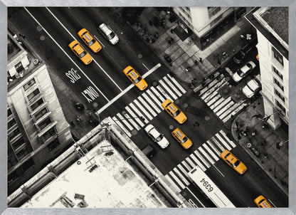 An aerial, black and white photograph of a bustling New York City intersection, with the iconic yellow taxi cabs highlighted in a vibrant selective color. Pedestrians cross the street as cars and a bus navigate the busy roads between tall buildings. Wall Art