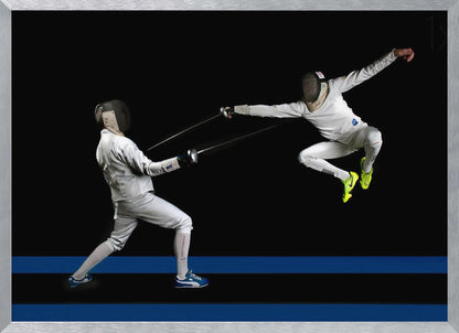 A dynamic action shot of two fencers in full white gear and masks dueling with foils against a stark black background. The fencer on the right is captured mid-air in a dramatic leap, while the fencer on the left lunges forward on a surface marked with blue lines. The image is enclosed in a silver frame. Artwork