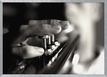 A dramatic, close-up, black and white photograph of a musician's fingers pressing down on the silver valves of a trumpet, with a soft, out-of-focus background. The image is enclosed in a brushed silver frame. Poster