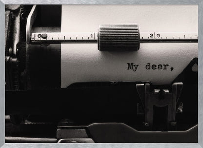 A close-up, black and white photograph of a vintage typewriter. A sheet of white paper is loaded, and the words 'My dear,' have just been typed, creating a sense of nostalgia and romance. The image is enclosed in a silver frame. Wall Art