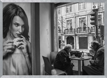 A framed, black and white photograph capturing a scene of juxtaposition. On the left, a large poster shows a glamorous young woman holding a coffee cup. On the right, seen through a cafe window, an elderly couple sits at a small table, also with coffee cups, engaged in conversation against a backdrop of an old European city street. Poster