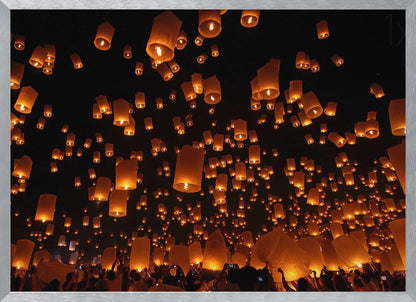 A framed photograph of a sky lantern festival at night, with hundreds of warm, orange-glowing lanterns floating up into the pitch-black sky from a crowd of people below. Artwork