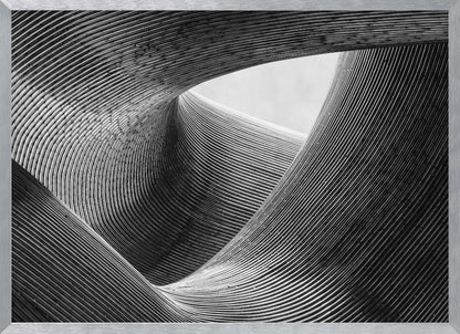 A framed, black and white abstract photograph of a swirling, textured structure. The low-angle shot looks up at curving walls made of thin, parallel lines, creating a dynamic sense of movement and depth, with an opening to a bright sky at the top. Artwork
