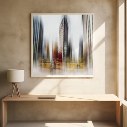 An artistic photograph of New York City's Flatiron Building in a light wood frame. The image has a strong vertical motion blur effect, creating streaks of yellow from taxi cabs and gray from the surrounding architecture, capturing the bustling energy of the city. Poster
