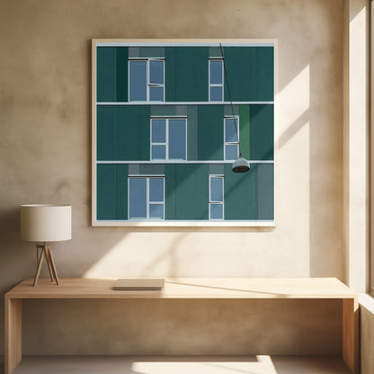 A framed photograph of a modern, dark green building facade with a grid of windows across three levels. A single industrial-style pendant lamp hangs in front of the building on the right side, interrupting the symmetrical pattern. The entire scene is enclosed by a light wood frame. Decor