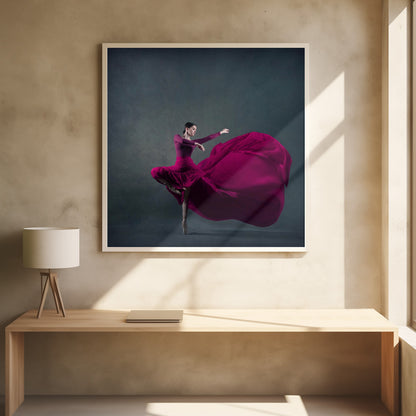 A graceful ballet dancer in a vibrant magenta dress strikes a pose on pointe, with the long, flowing fabric of her skirt billowing out dramatically behind her against a dark, textured gray background, all enclosed in a simple light wood frame. Decor