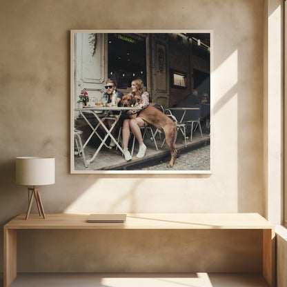 A framed photograph of a young couple sitting at an outdoor cafe. A woman in a floral shirt holds a large brown Rhodesian Ridgeback on her lap, while a man in sunglasses sits beside her. The dog stands with its front paws on the woman's lap and back paws on the wooden deck. The scene has a muted, warm tone. Poster