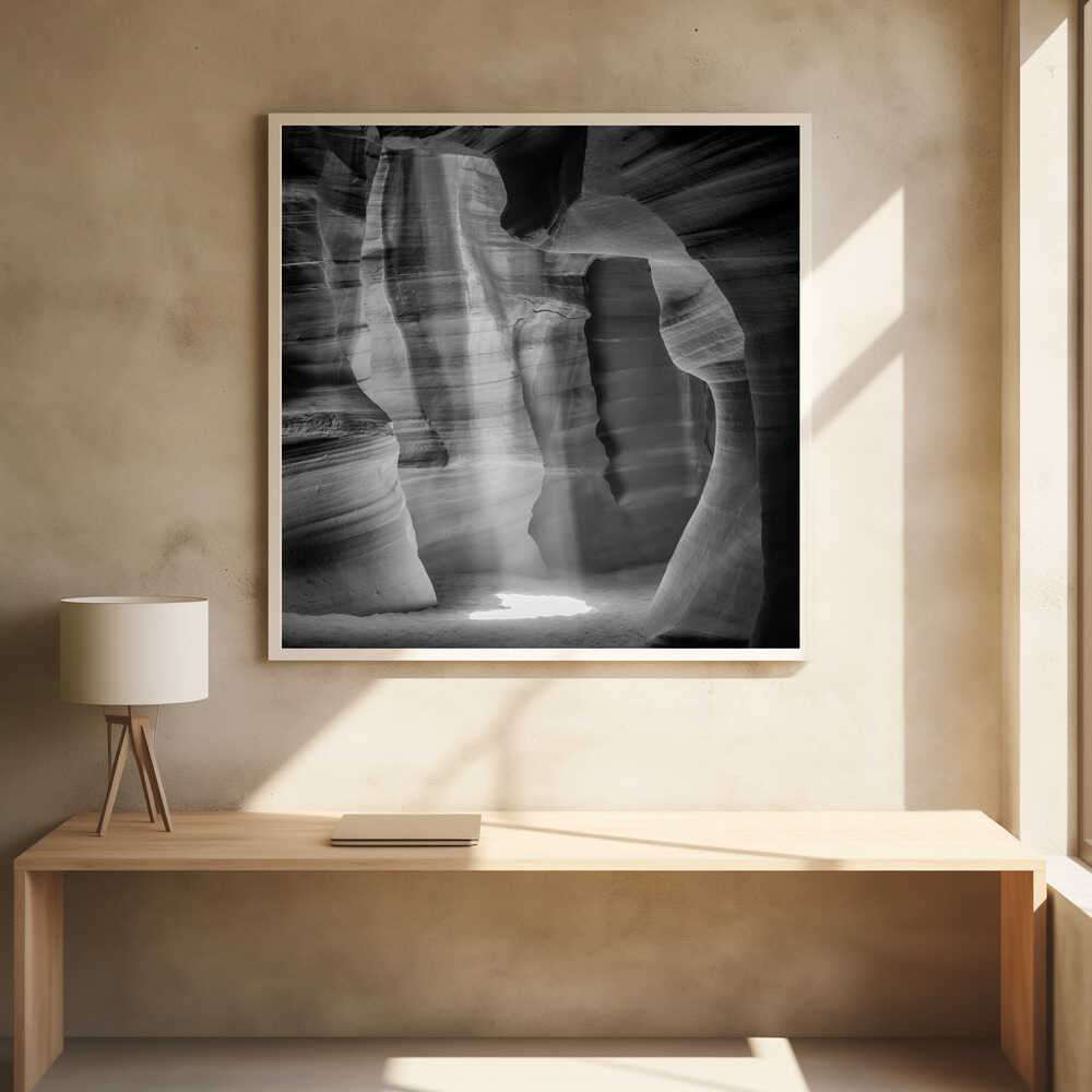 A dramatic black and white photo of a sunbeam lighting the sandy floor of a smooth, curved slot canyon.