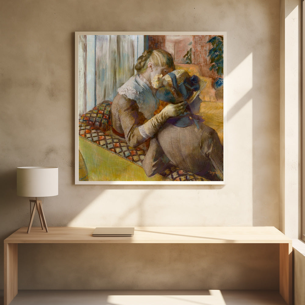 A framed Impressionist painting by Edgar Degas depicting two women. One woman, with blonde hair tied back, adjusts a hat with a blue ribbon on the other woman who is sitting with her back mostly to the viewer on a colorful patterned sofa. Print