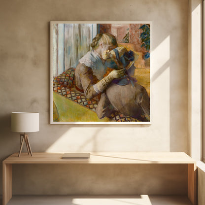 A framed Impressionist painting by Edgar Degas depicting two women. One woman, with blonde hair tied back, adjusts a hat with a blue ribbon on the other woman who is sitting with her back mostly to the viewer on a colorful patterned sofa. Print