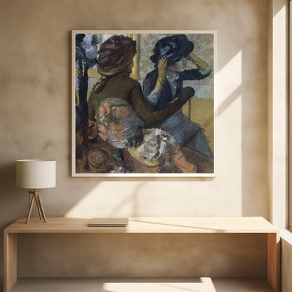 A framed impressionist painting by Edgar Degas, 'The Millinery Shop', depicting two women. One woman, seen from the back, wears a brown coat and hat, while the other tries on a dark blue hat, adjusting it with her gloved hands. Colorful hats are displayed in the foreground. Print