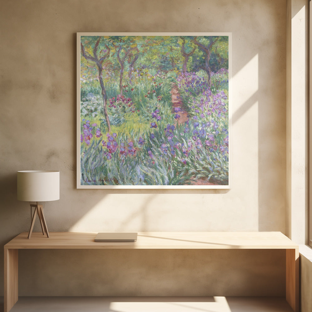 An impressionist painting by Claude Monet, 'The Artist's Garden at Giverny,' set in a light wood frame. The artwork depicts a lush, vibrant garden with a path winding through it. The foreground is dominated by purple irises and tall green leaves, while the background features trees and a mix of colorful flowers in shades of red, yellow, and white, all rendered with visible, textured brushstrokes. Print