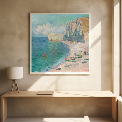 An impressionist painting by Claude Monet depicting the beach at Étretat, France, enclosed in a light wood frame. The artwork shows tall, light-colored cliffs on the right, a sandy beach with small boats, and vibrant turquoise water with a few red-sailed boats. The sky is partly cloudy. Decor
