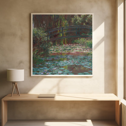 An impressionist painting by Claude Monet of the Japanese bridge over his water lily pond. The artwork, framed in light wood, is rich with shades of green from the foliage and lily pads, and deep brown and blue tones in the water and the bridge itself. Wall Art