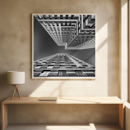A framed, black and white, low-angle photograph looking up between two towering skyscrapers, creating a dramatic perspective with geometric patterns against a dark sky. Poster